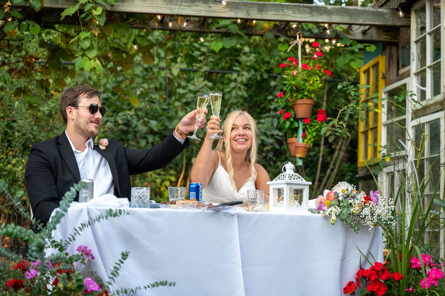 Couple toasting champagne at elegant outdoor garden wedding reception with floral decorations.