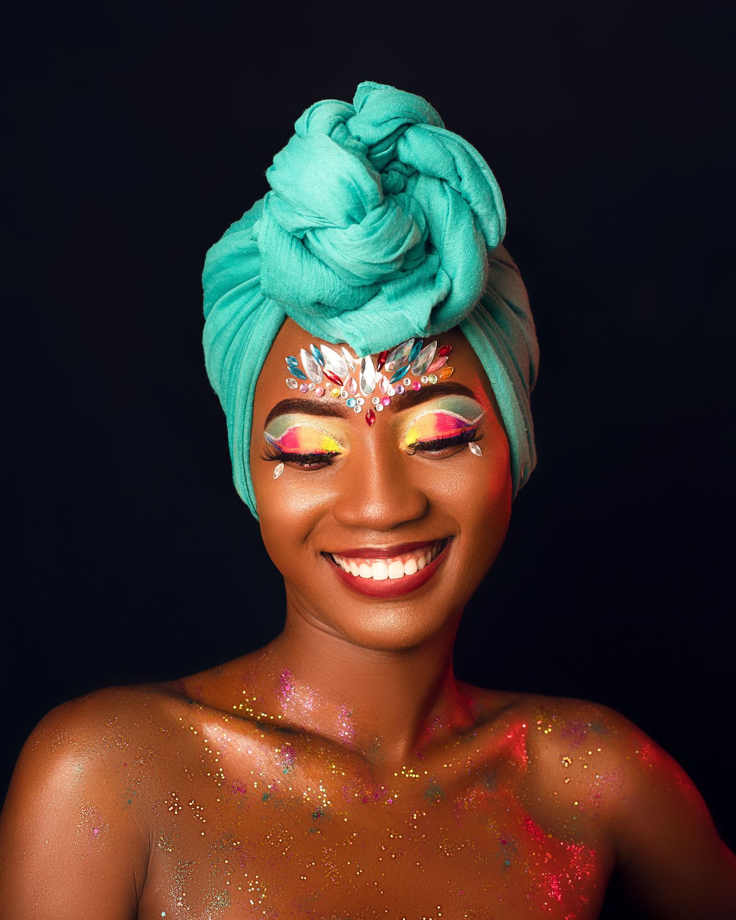 A portrait with turquoise head wrap, vibrant eye makeup, and shimmering glitter details against a dark background.