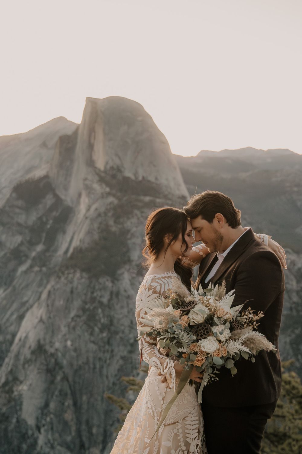 A couple shares an intimate moment with a bouquet against the backdrop of Half Dome in Yosemite.