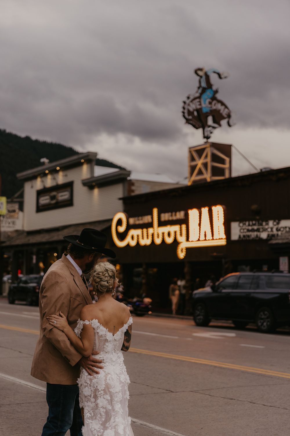 A couple shares an intimate moment in front of the Cowboy Bar sign during sunset in Jackson Hole, Wyoming.