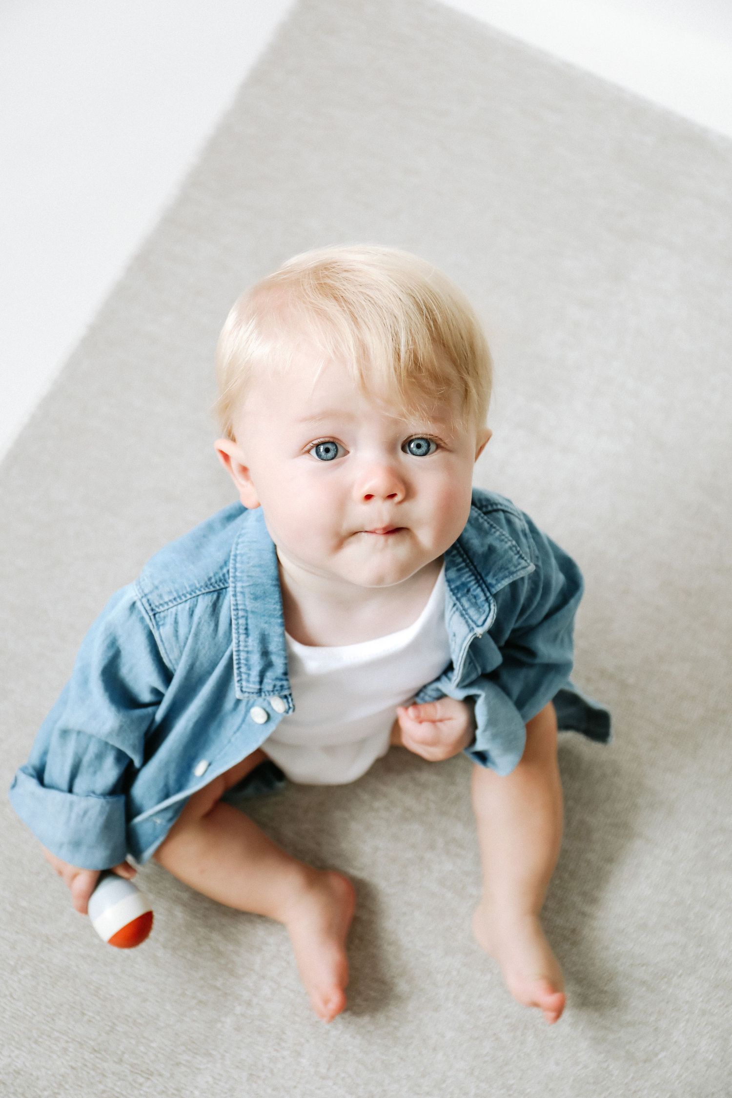 Small child sitting on gray floor wearing denim jacket and white shirt with bright blue eyes.