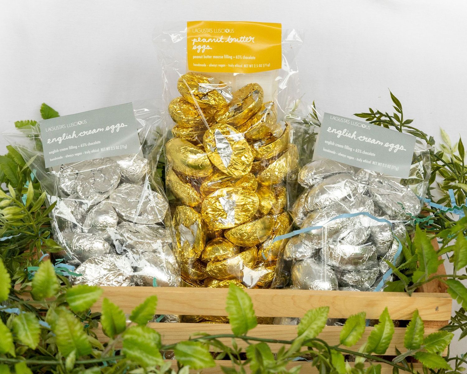 Gold and silver foil wrapped chocolates displayed in a wooden crate surrounded by greenery.