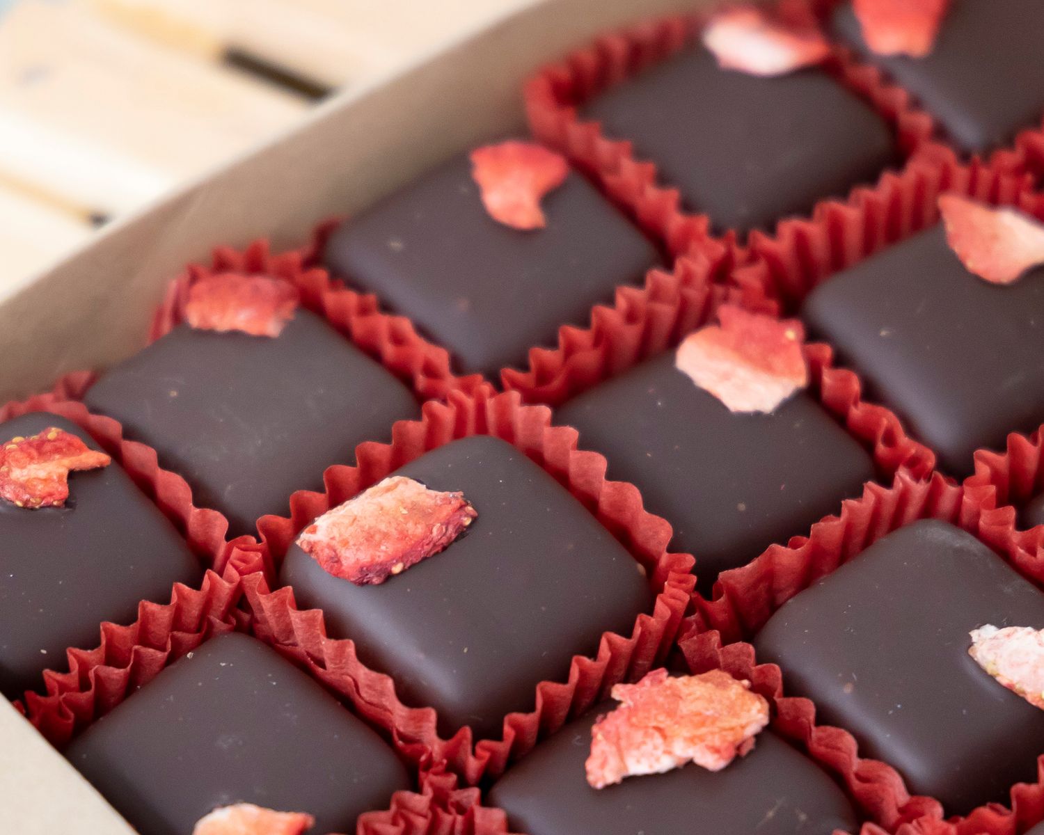 Dark chocolate petit fours decorated with red icing borders and pink candied rose petals arranged in paper cups.