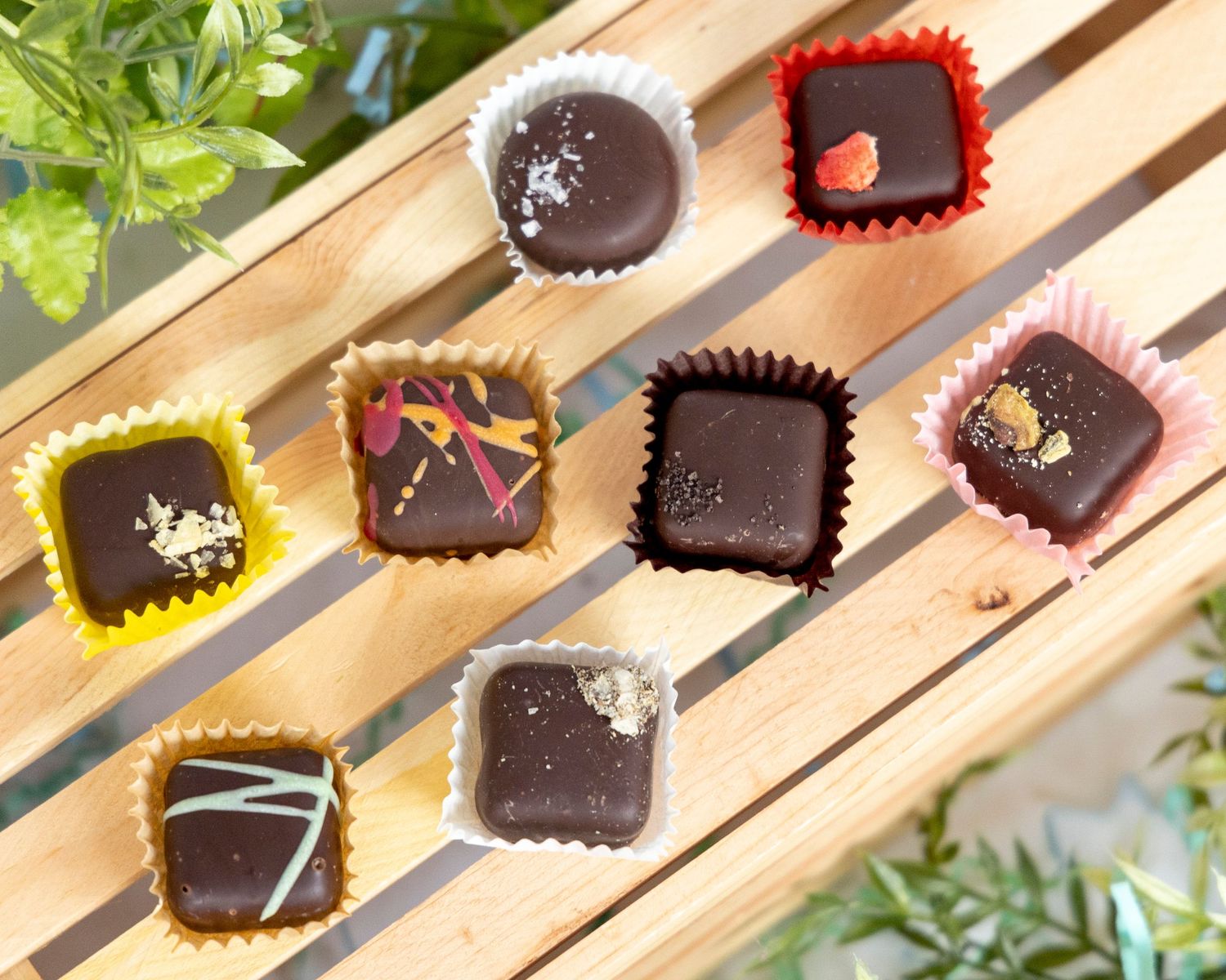 Artisanal chocolate bonbons with colorful decorative wrappers arranged on a wooden surface.