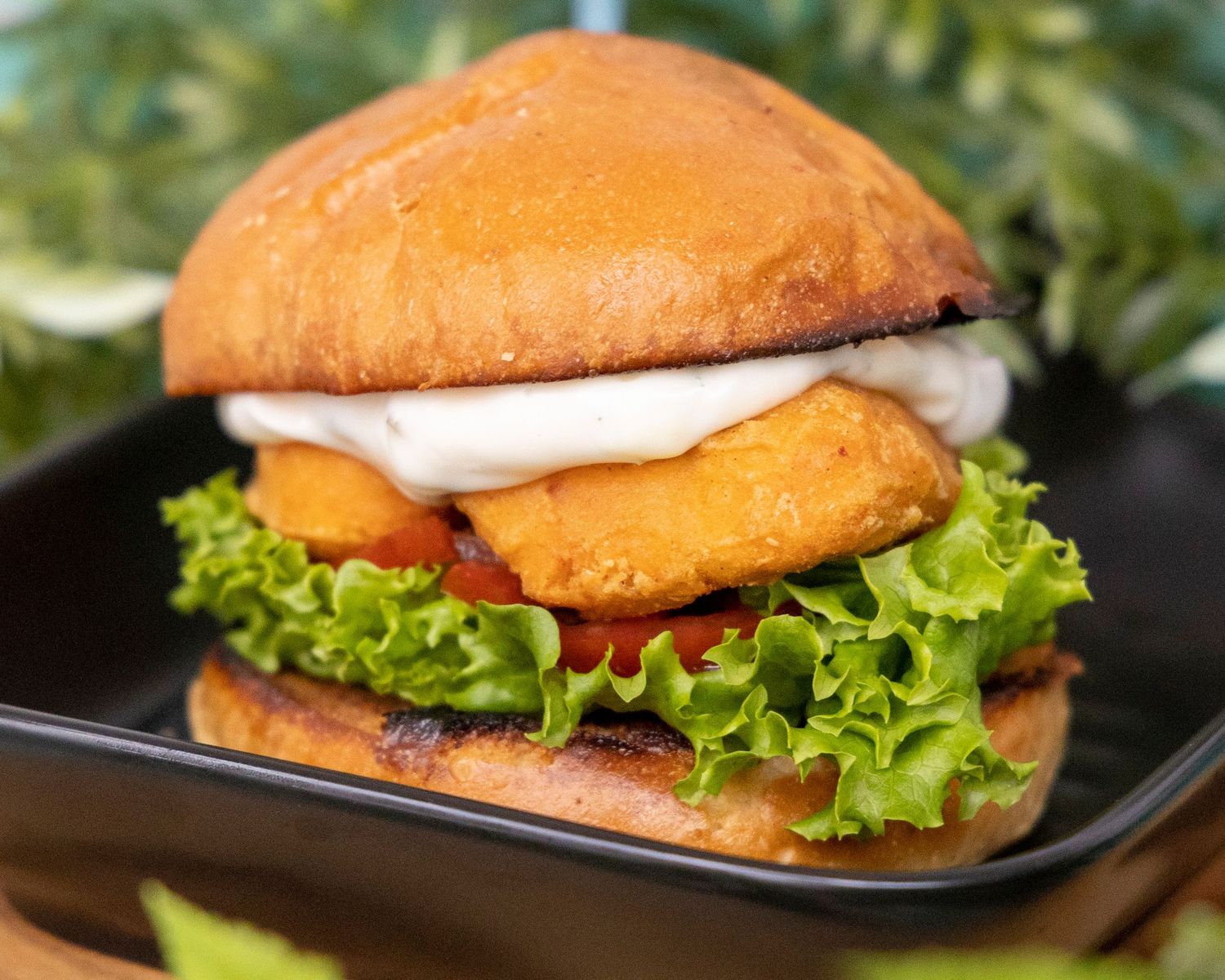 A crispy fried chicken sandwich with lettuce and onions served on a golden brioche bun on a black plate.