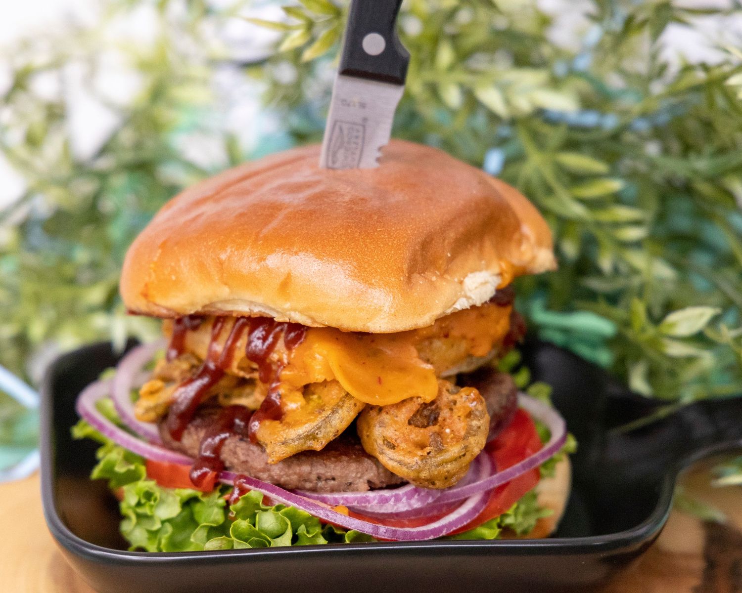 Close-up of gourmet cheeseburger with caramelized onions and crisp lettuce on a black plate.