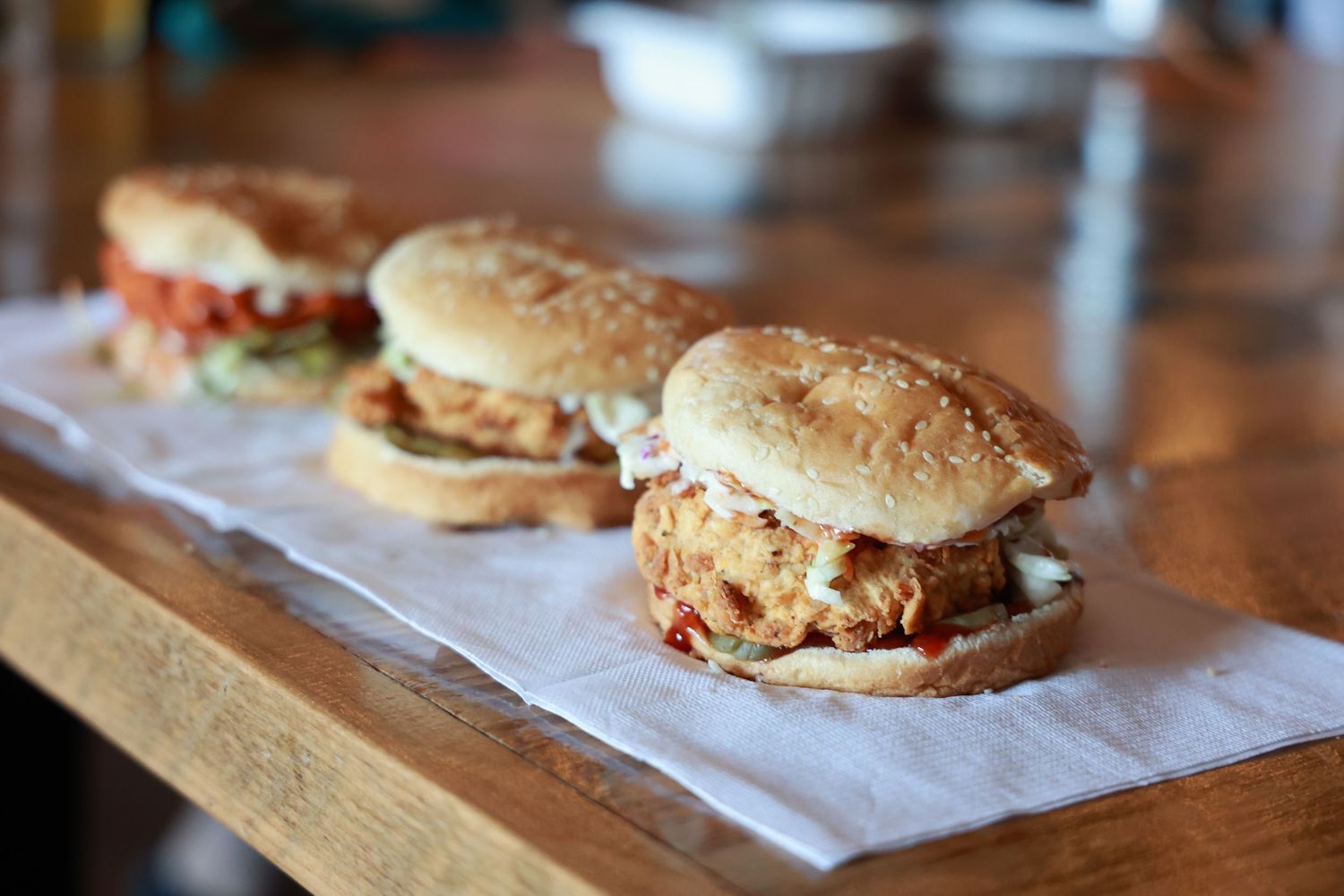 A BBQ chicken sandwich topped with melted cheese and corn on a toasted bun sits on parchment paper.