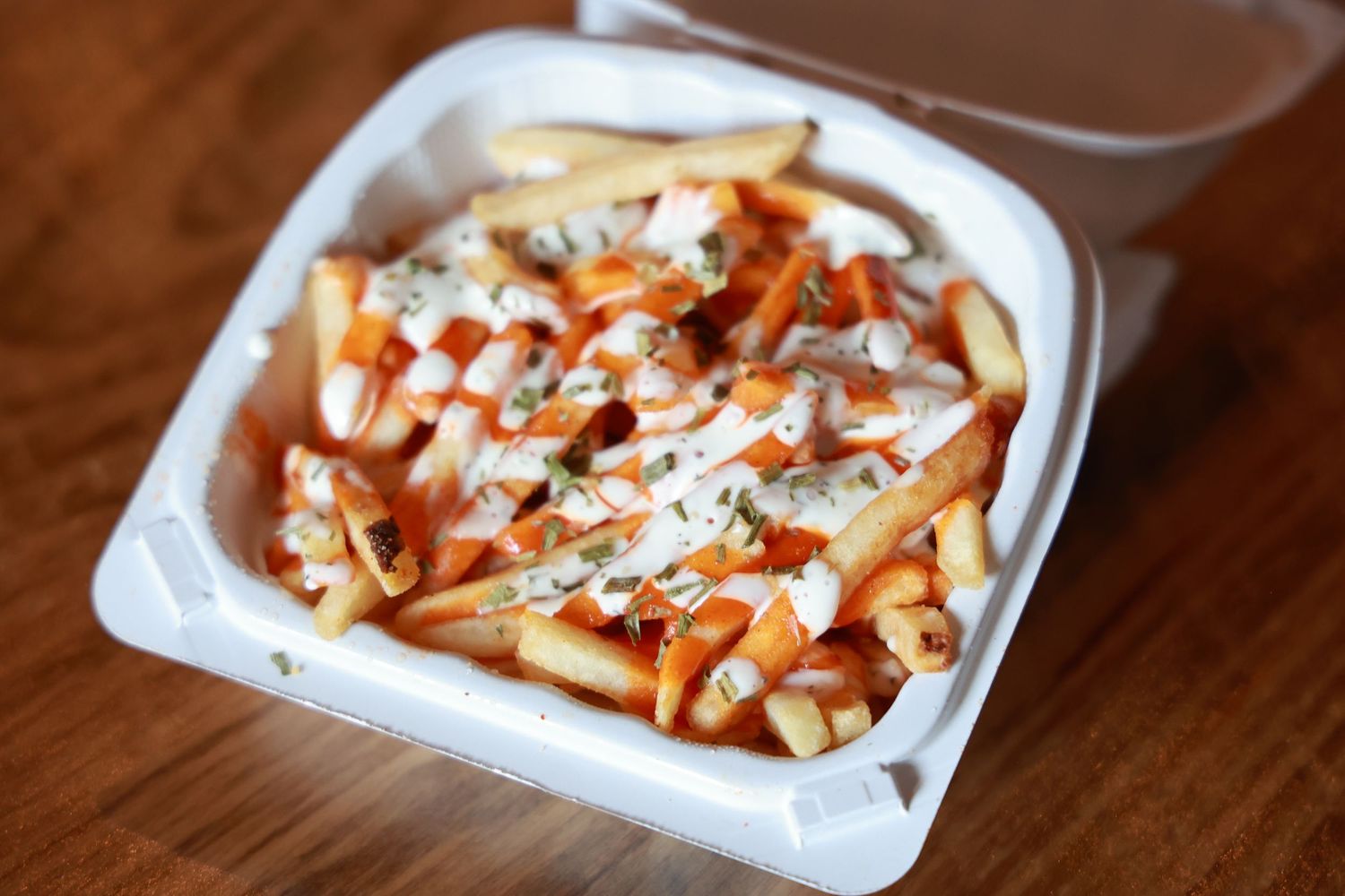 A takeout container filled with crispy french fries topped with buffalo sauce and blue cheese crumbles.