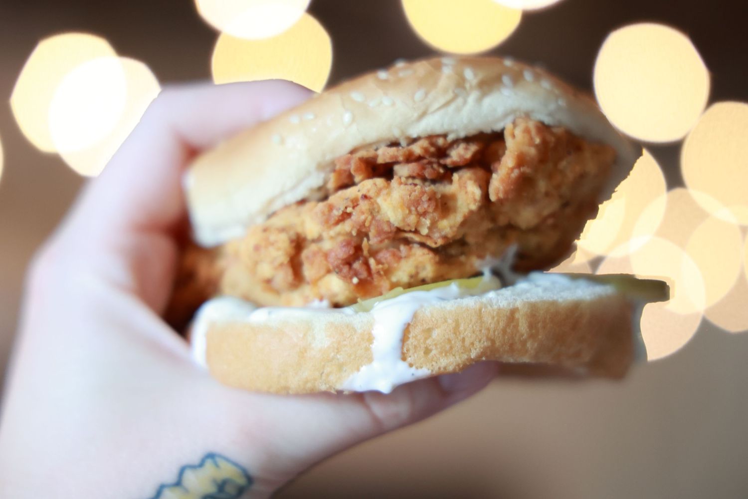 A crispy chicken sandwich on a soft white bun photographed with bokeh lights in the background.
