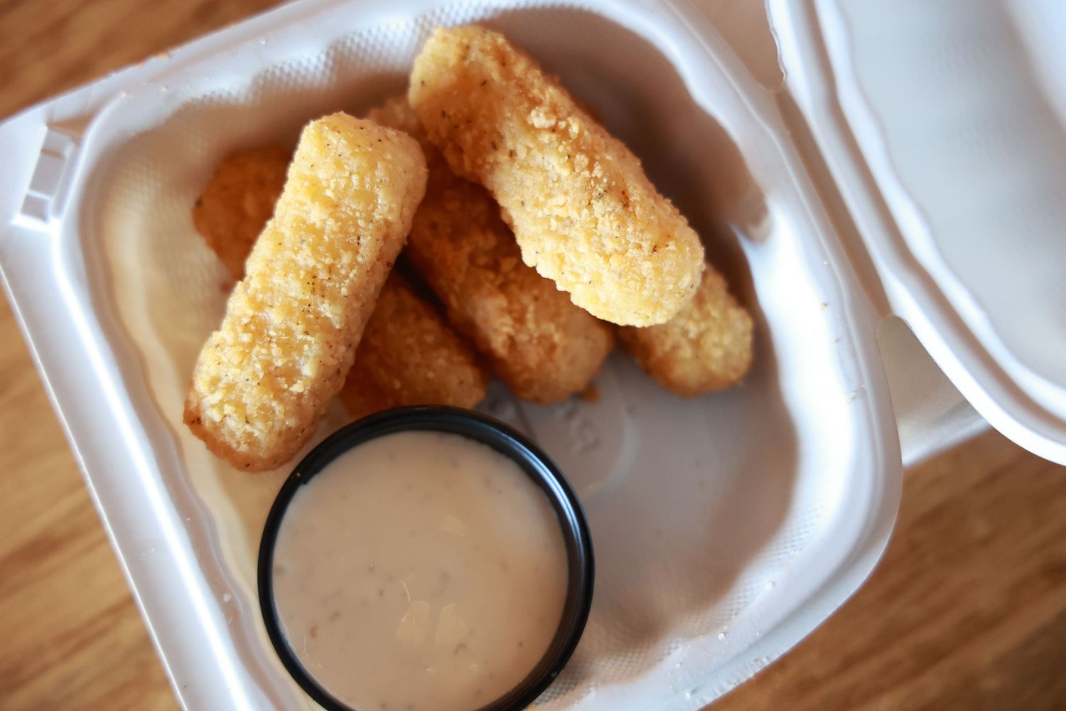 Golden brown chicken fingers served with creamy dipping sauce in a white takeout container.