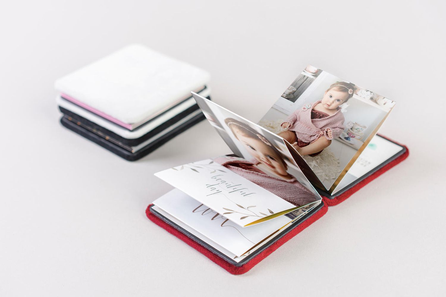 Several compact mini photo albums in white, black and red colors displayed with one open to show printed photographs inside.