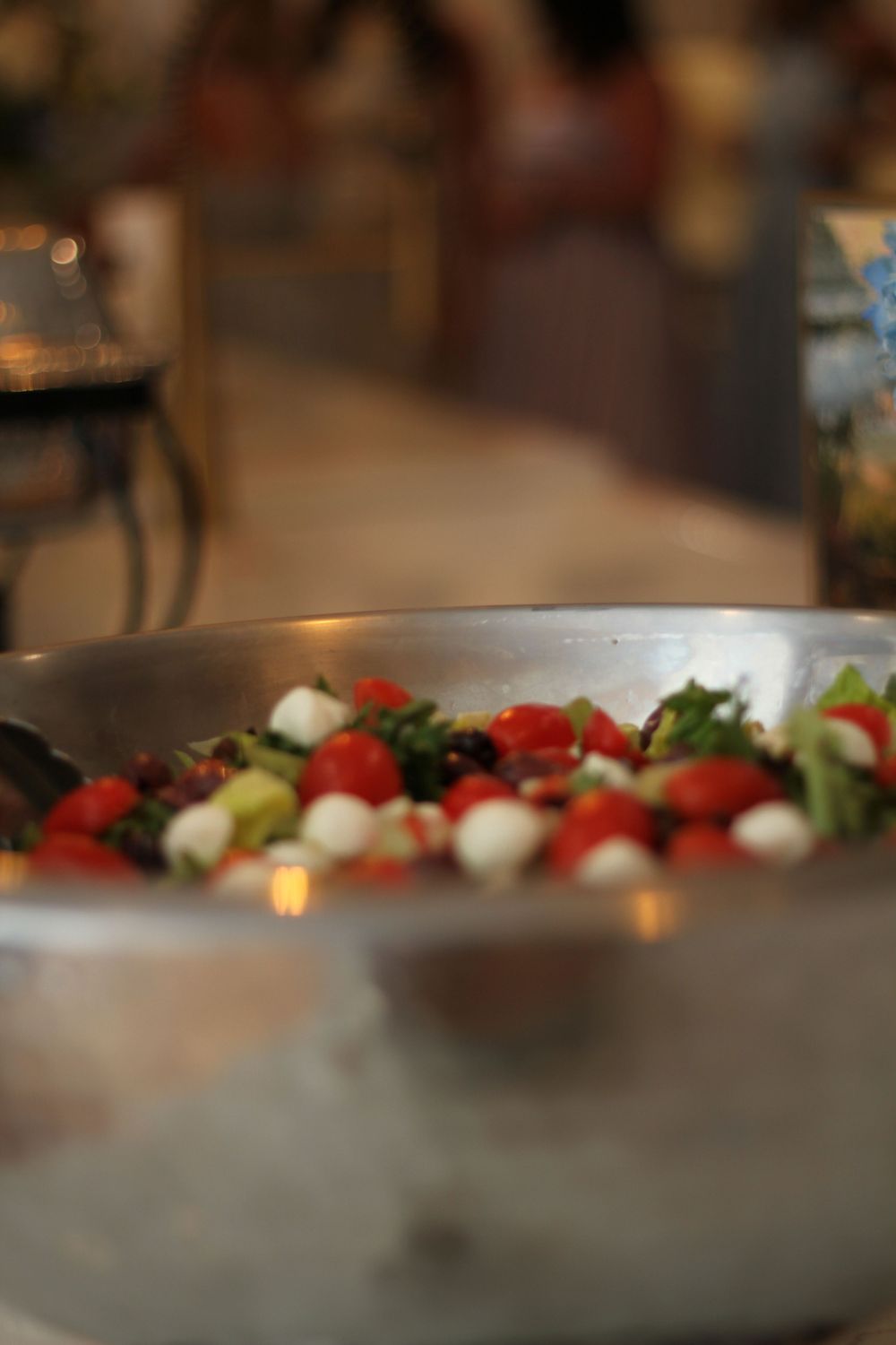 A shallow depth of field close-up view of fresh caprese salad with cherry tomatoes and mozzarella in a metal bowl.