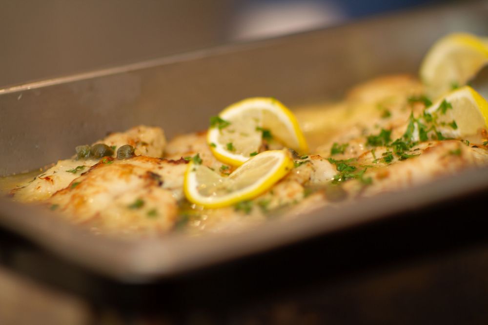 A close-up sequence of baked fish with lemon slices and fresh herbs served on a white plate.