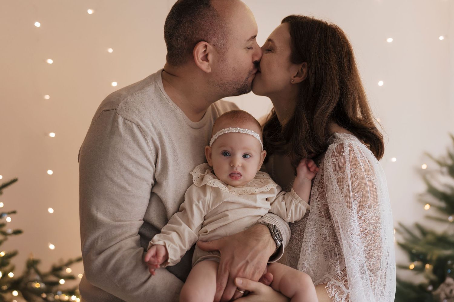 A romantic family photoshoot with twinkling lights and evergreens creates a cozy winter holiday atmosphere.
