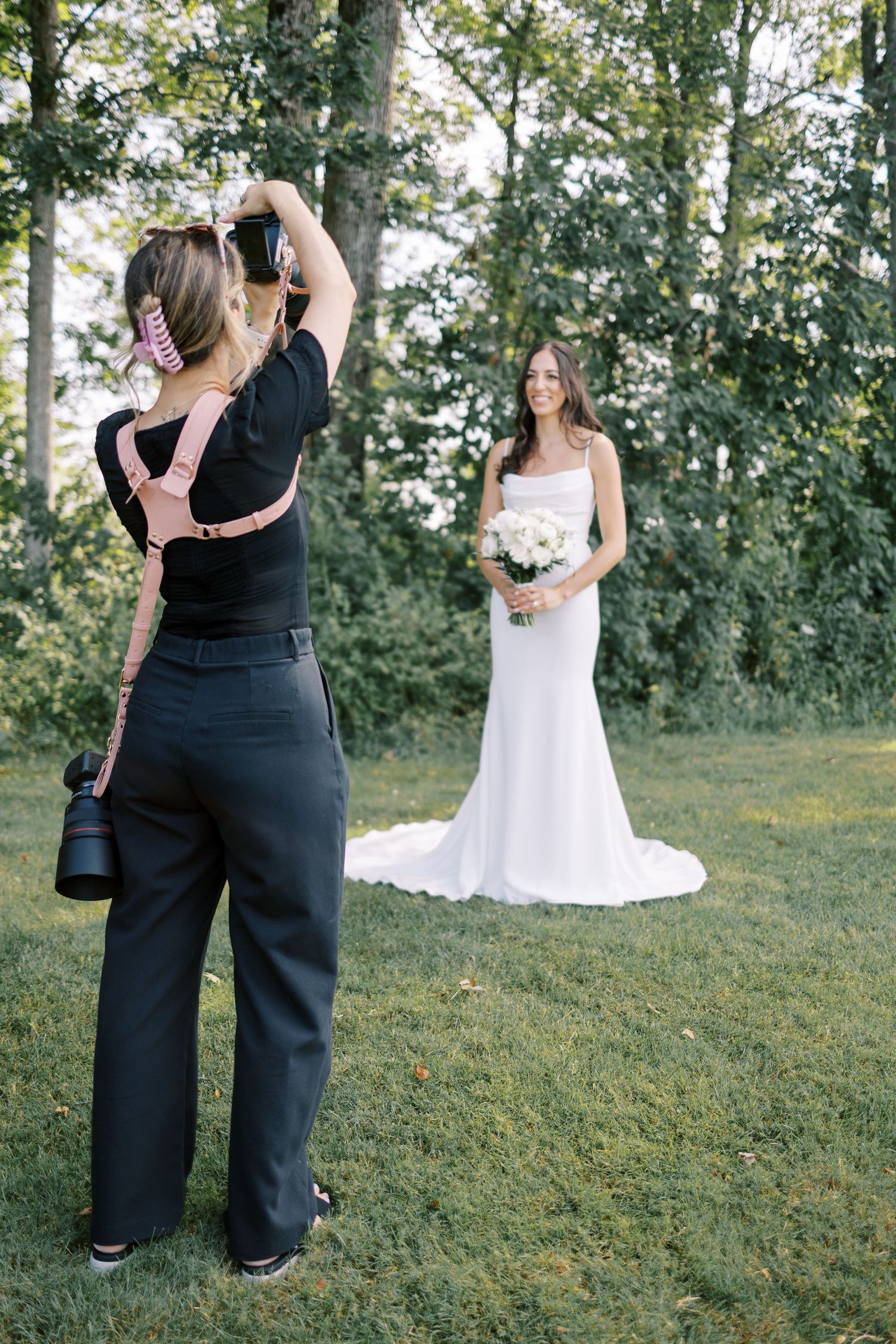 Photography capturing a wedding photographer at work taking photos of a bride in a white gown in an outdoor garden setting.