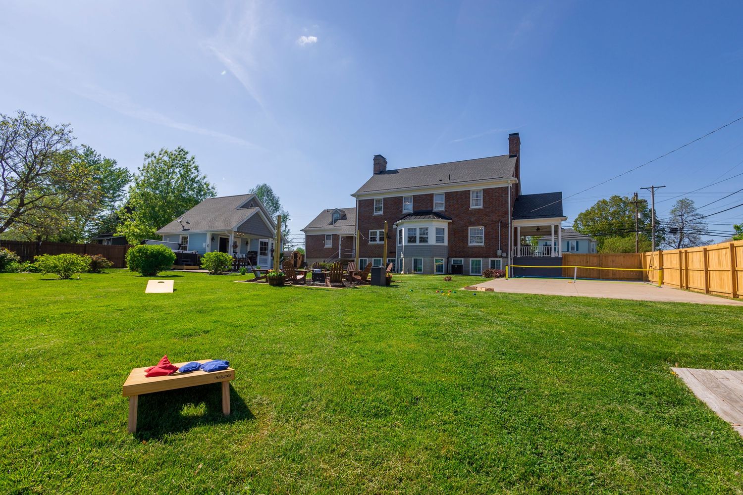 Spacious backyard lawn with brick houses and cornhole game board under blue sky.