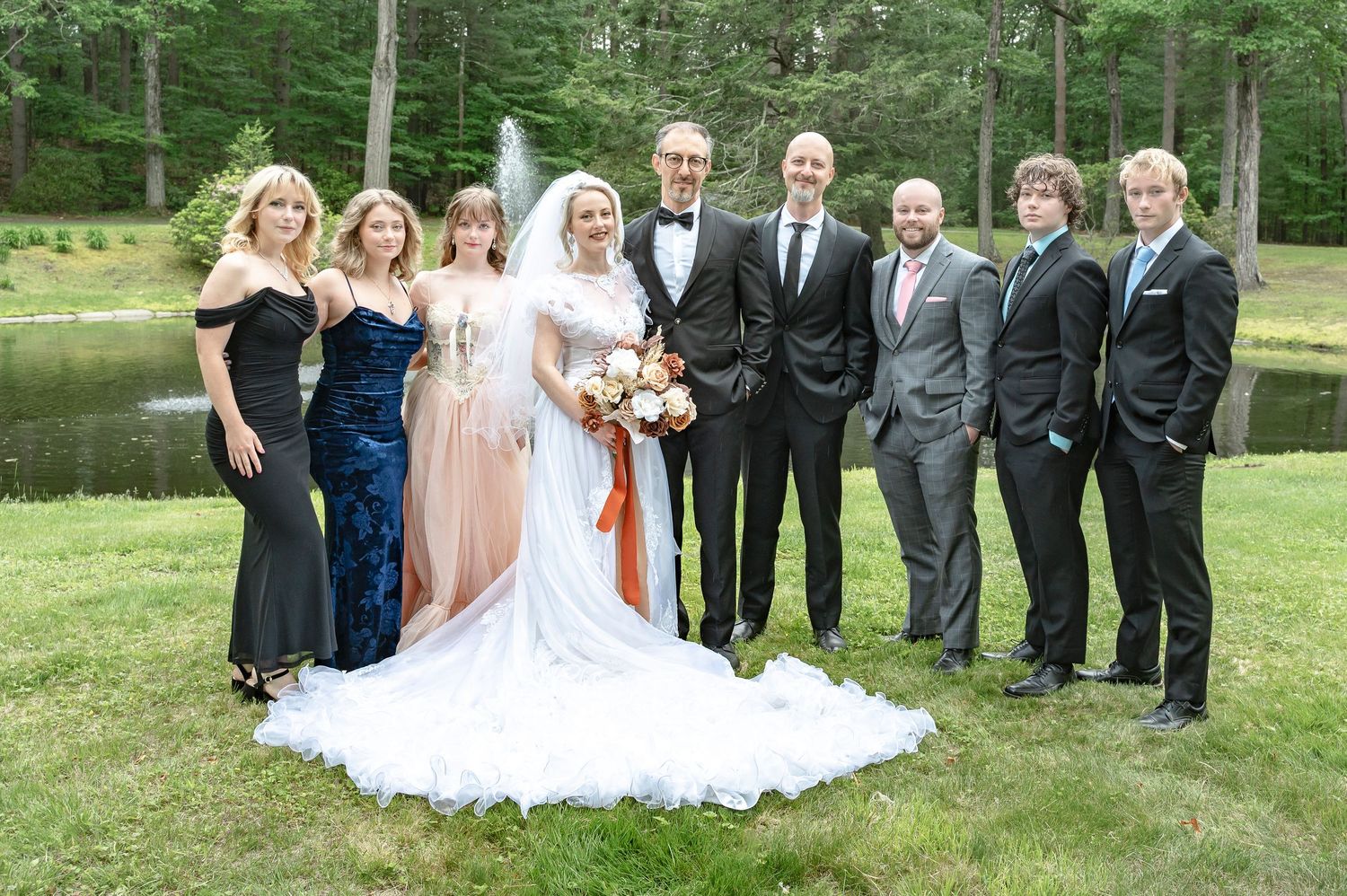 Wedding party poses outdoors in formal attire with trees in background.