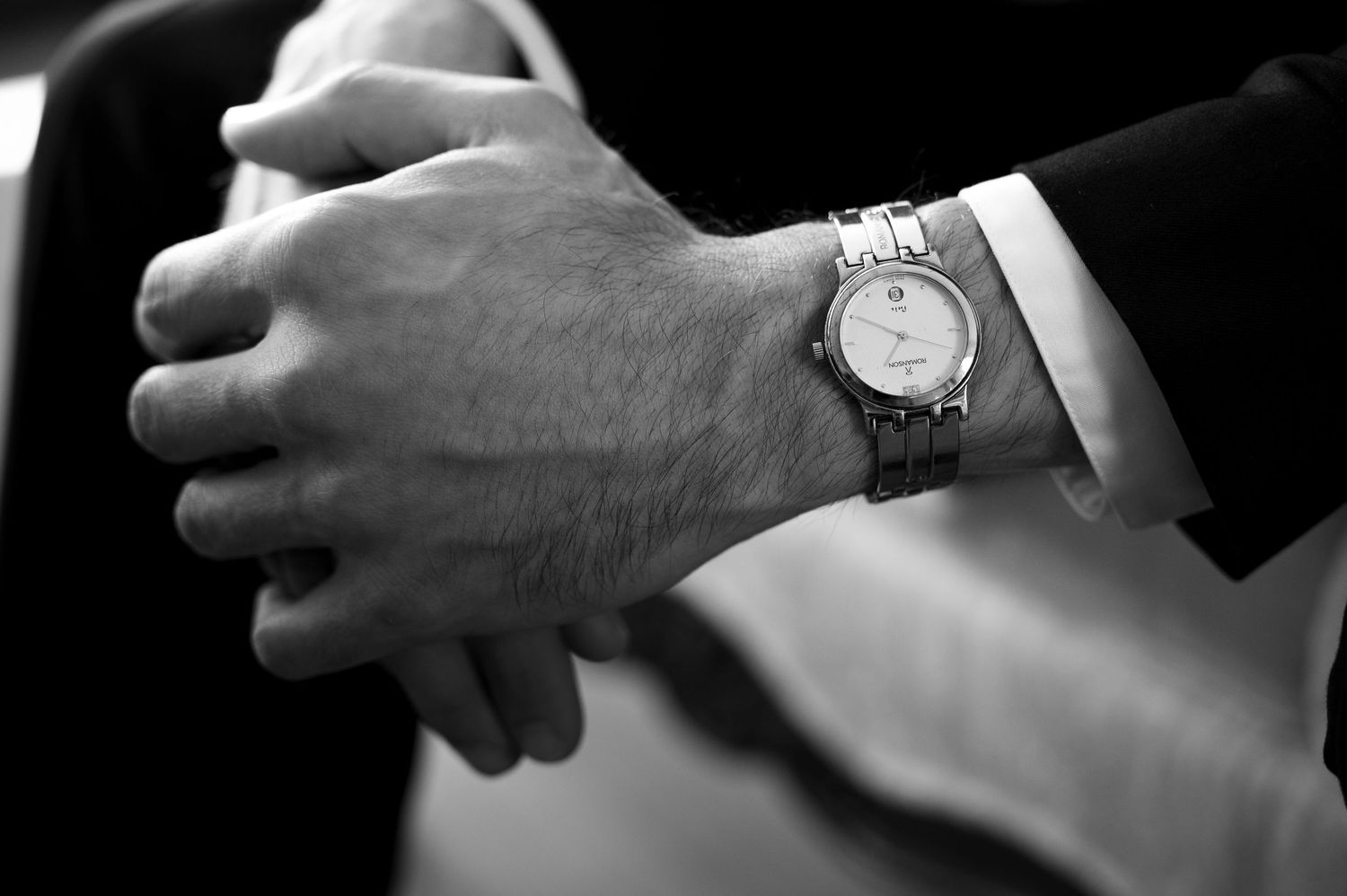 Black and white detail shot of hands and wristwatch during wedding ceremony.