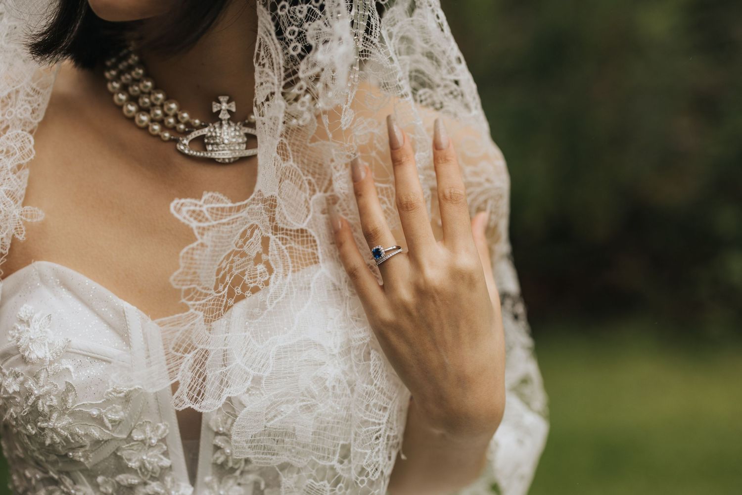 A close-up detail of an elegant lace wedding dress with a sparkling engagement ring and crystal jewelry.