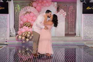 Couple sharing a kiss on the dance floor in front of a pink balloon and floral baby shower backdrop.
