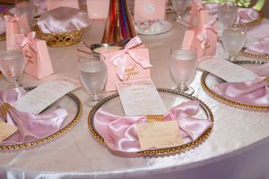 Elegant pink and gold baby shower table setting with satin napkins, gift boxes, and menu cards.