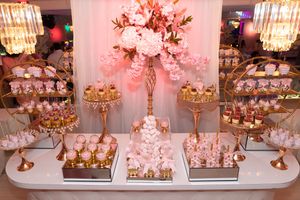 Stunning pink and gold dessert table with floral centerpiece, macarons, and tiered cake displays.