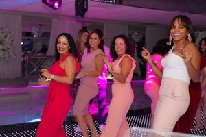 Four women dancing and smiling together on a dance floor at a festive pink-themed party event.