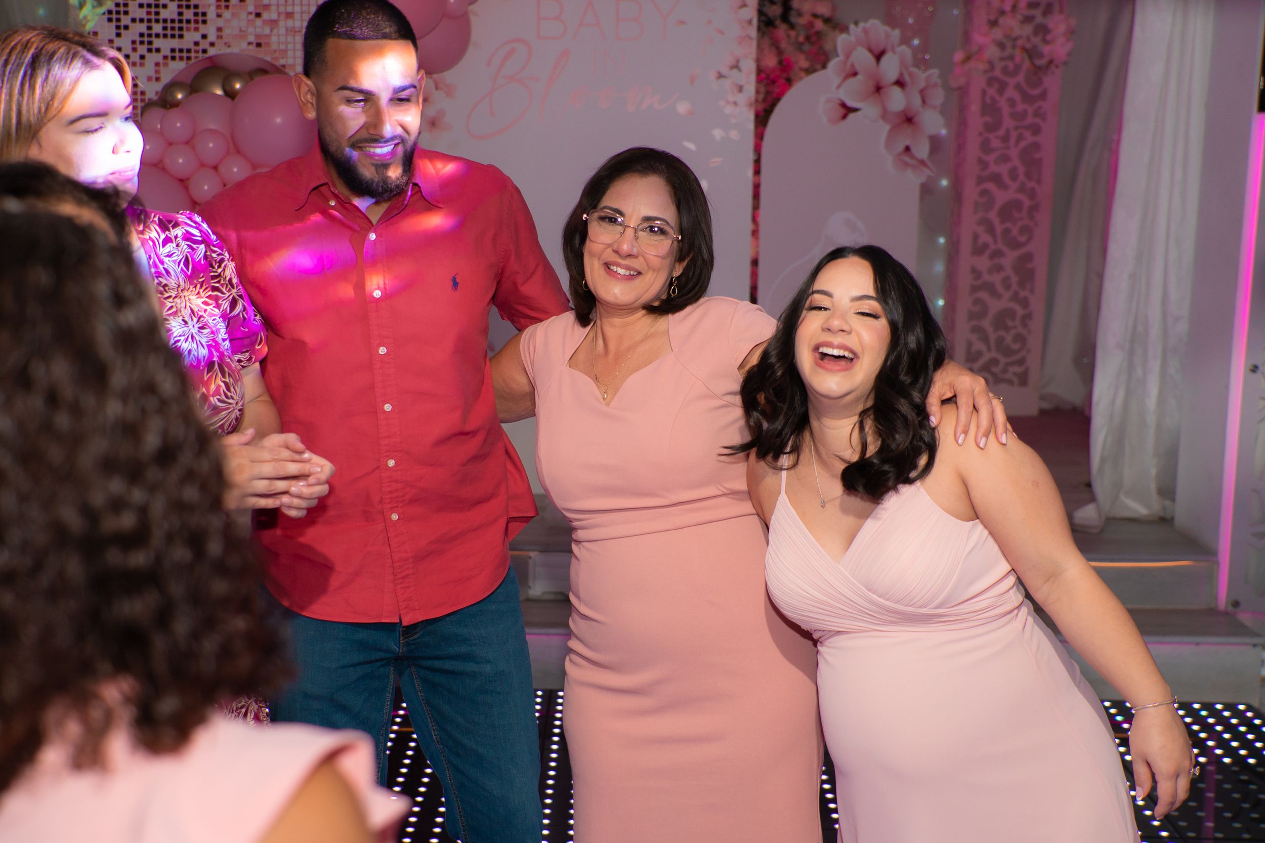 Group of guests laughing and posing together on the dance floor at a pink baby shower celebration.