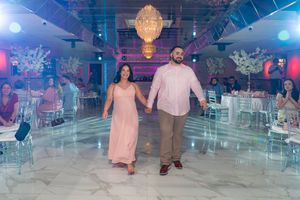 Couple holding hands walking onto a marble dance floor at an elegant pink-themed baby shower venue.