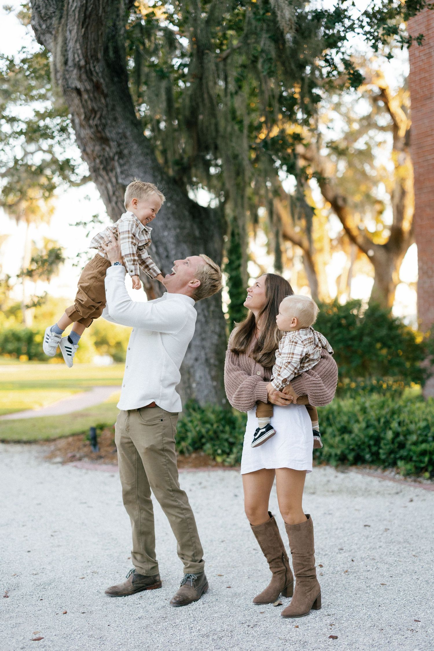 Family walking together on a winding sandy path through a tranquil park with sunlight filtering through oak trees.