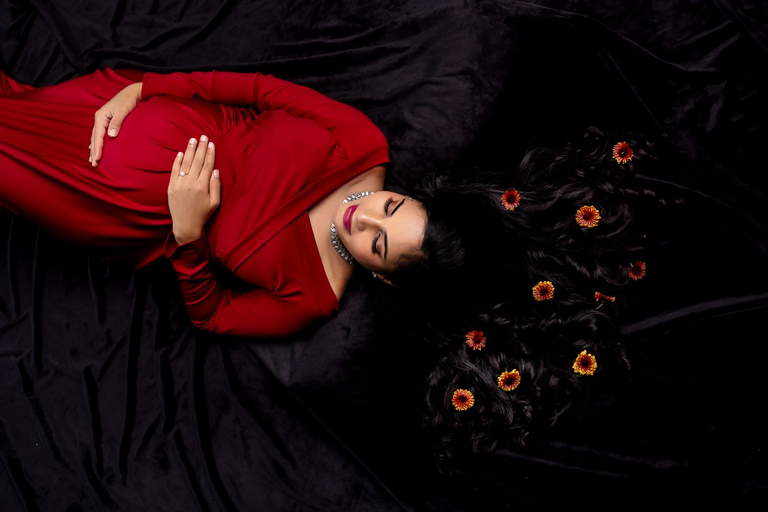 A figure in a red sweater lies on a black surface surrounded by scattered orange flowers.