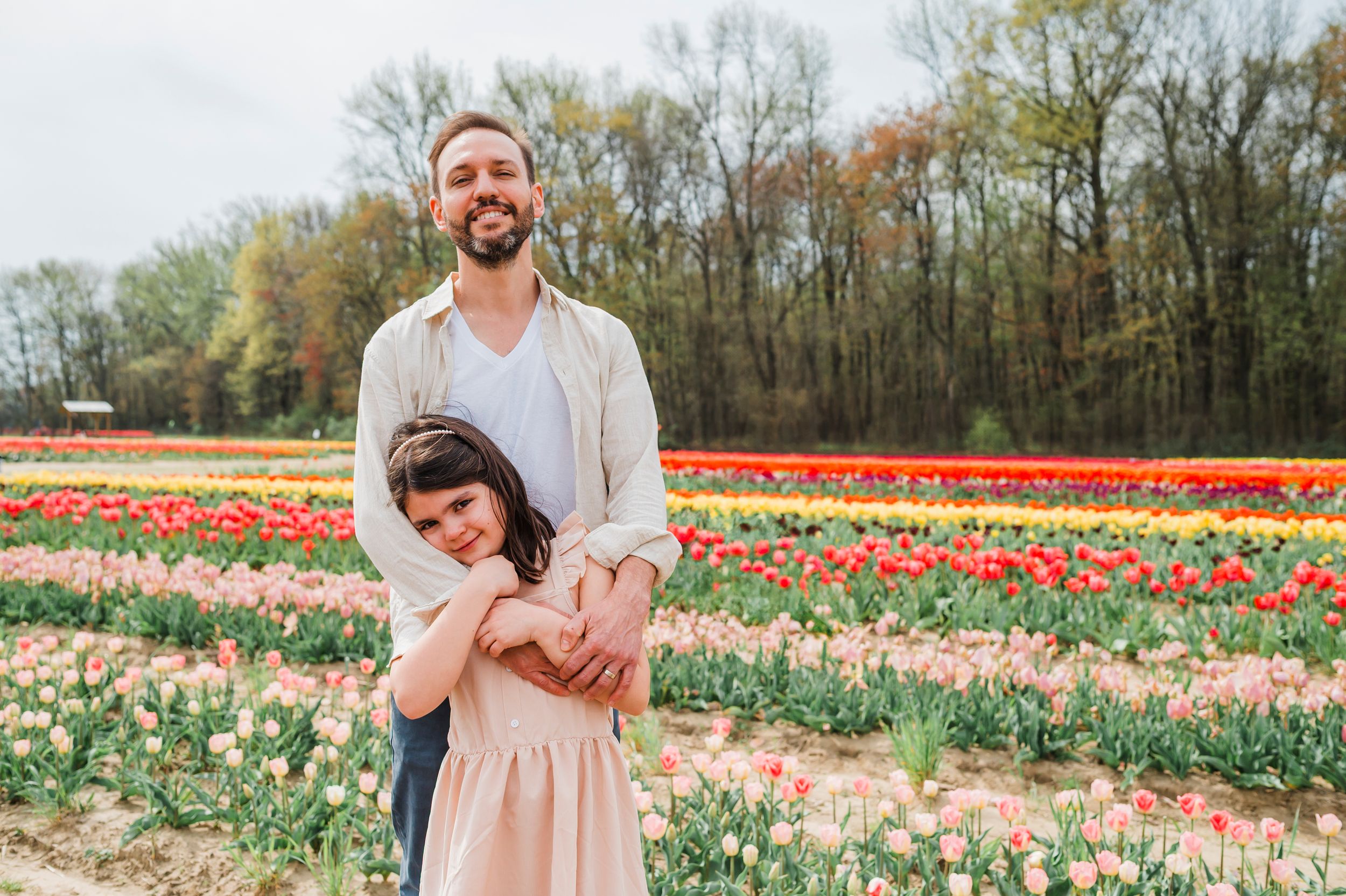Two people embrace while standing in a colorful springtime tulip field with trees in the background.