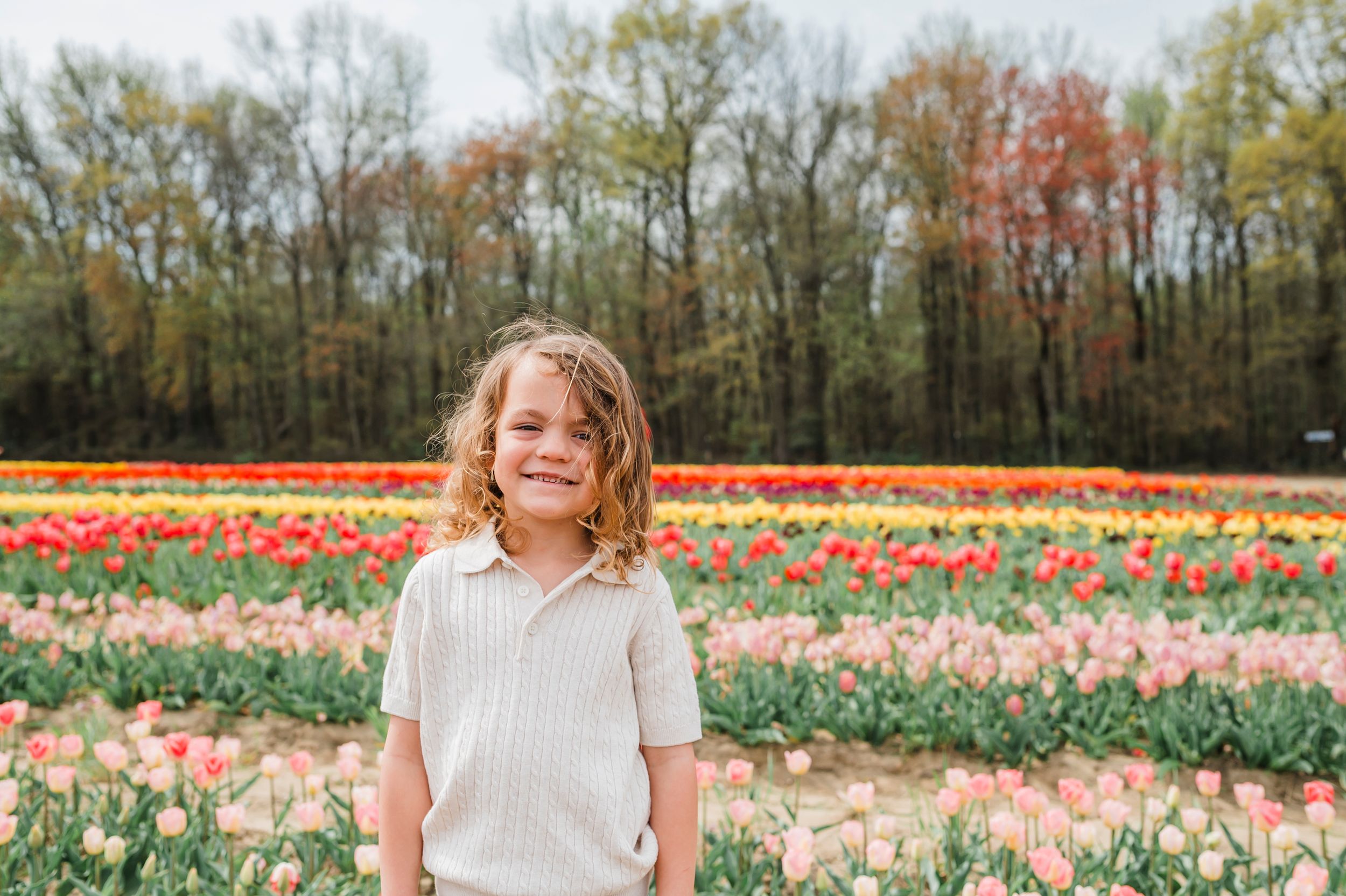 A beautiful tulip field in bloom with vibrant orange and pink flowers stretches behind a visitor on a spring day.