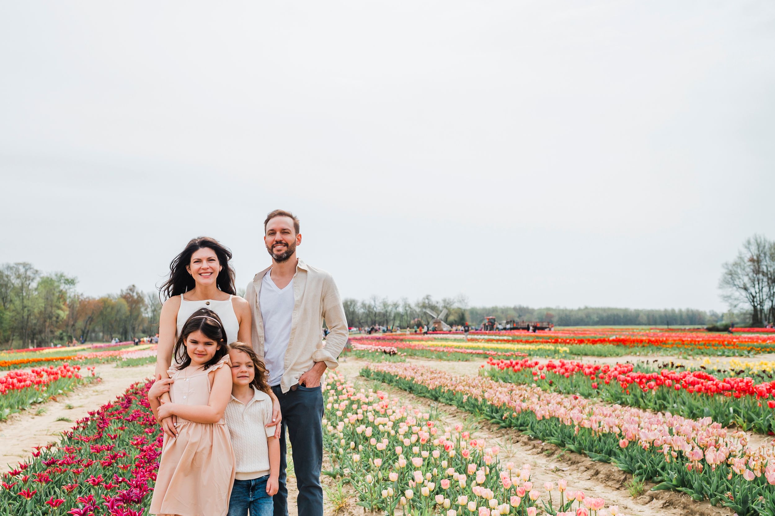People enjoy a spring day at a colorful tulip farm with rows of vibrant red, white and pink flowers stretching into the distance.