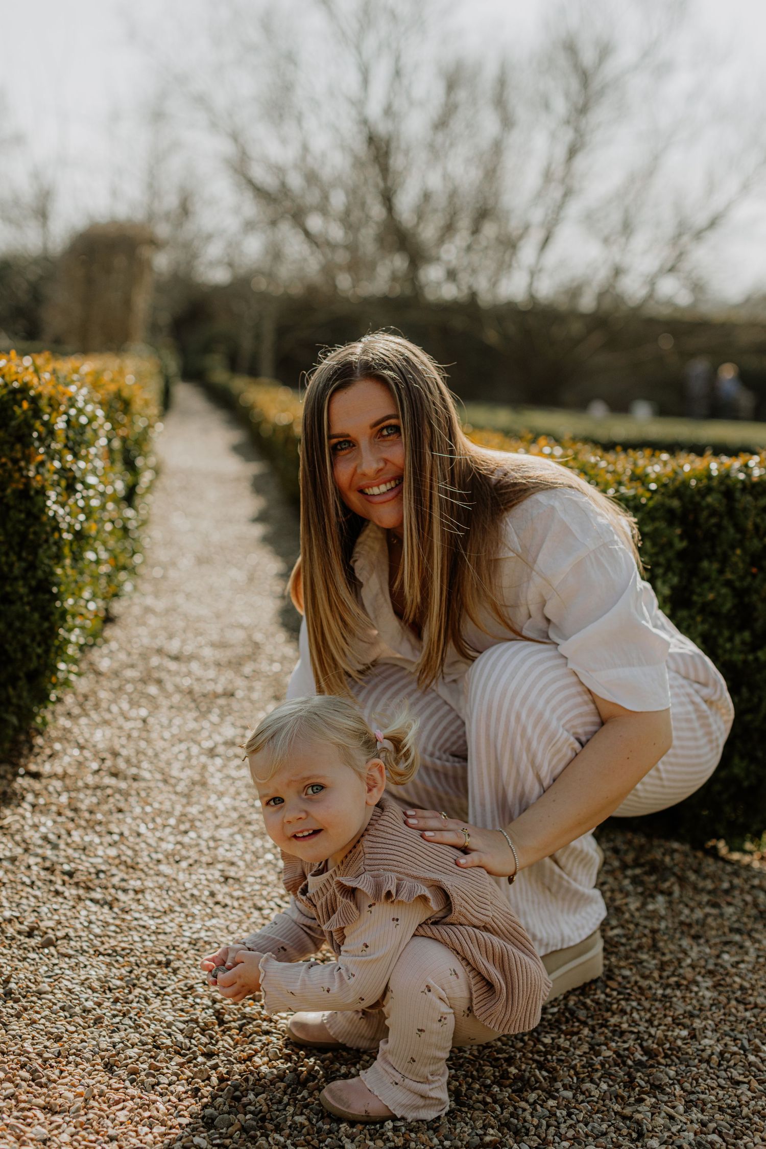 A tender moment captured in a garden as two people share a sweet interaction on a gravel path.