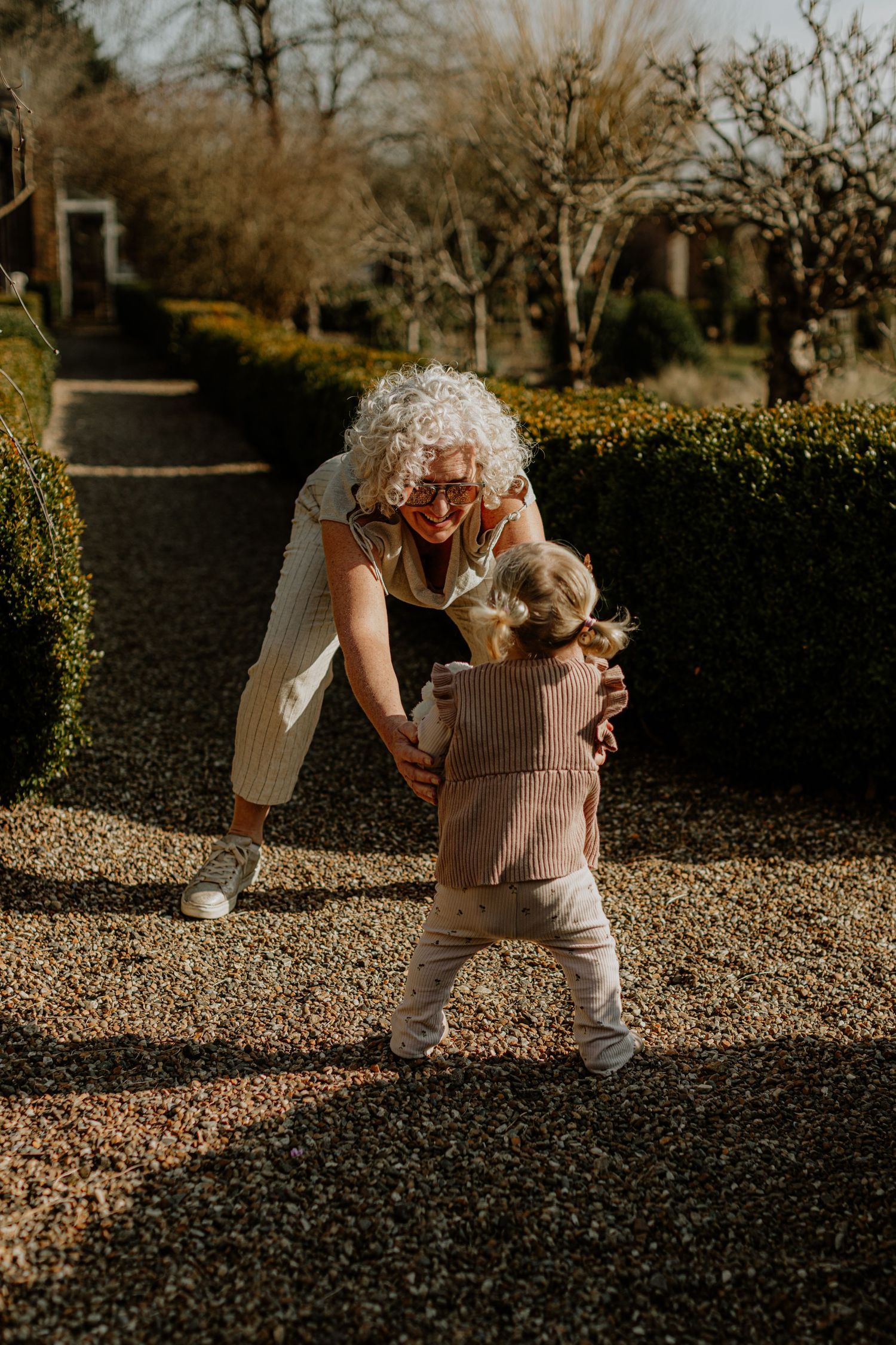 A heartwarming interaction between two people playing in a formal garden with manicured hedges.