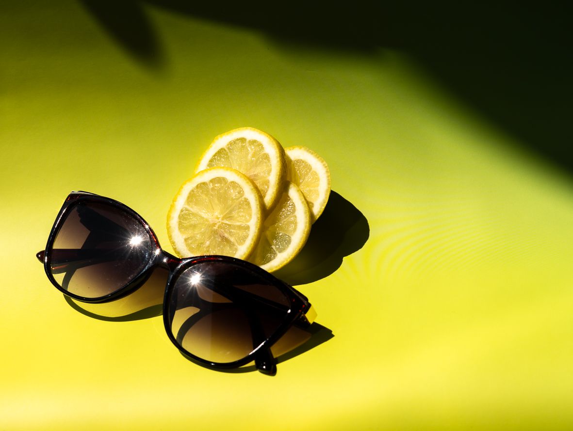 Black sunglasses with yellow lemon slices against a bright yellow background for a summer fashion concept.
