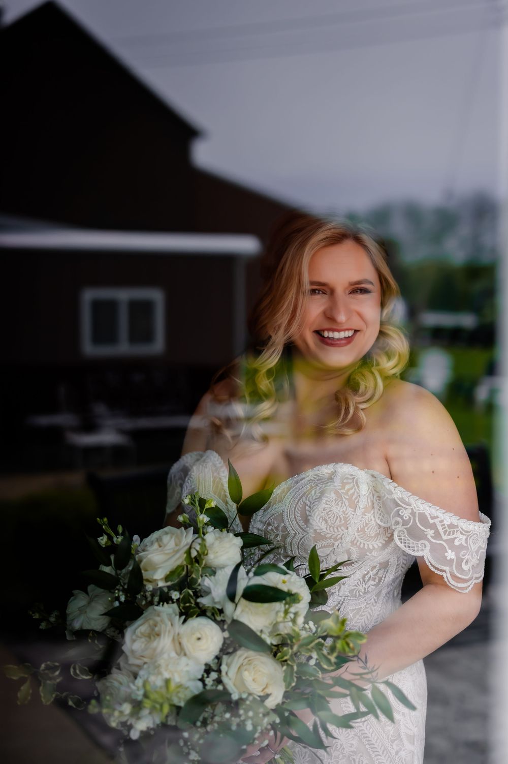 Radiant bride in off-shoulder lace gown holds elegant white and green floral bouquet during outdoor wedding shoot.