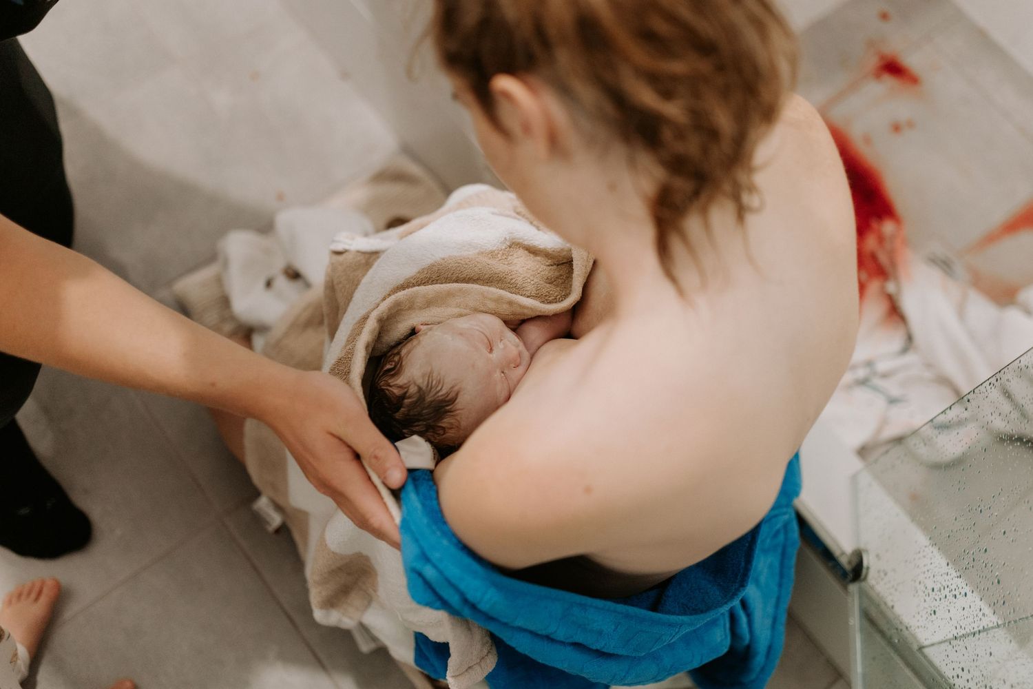 A newborn baby lies swaddled in white cloth and towels during an intimate childbirth moment.