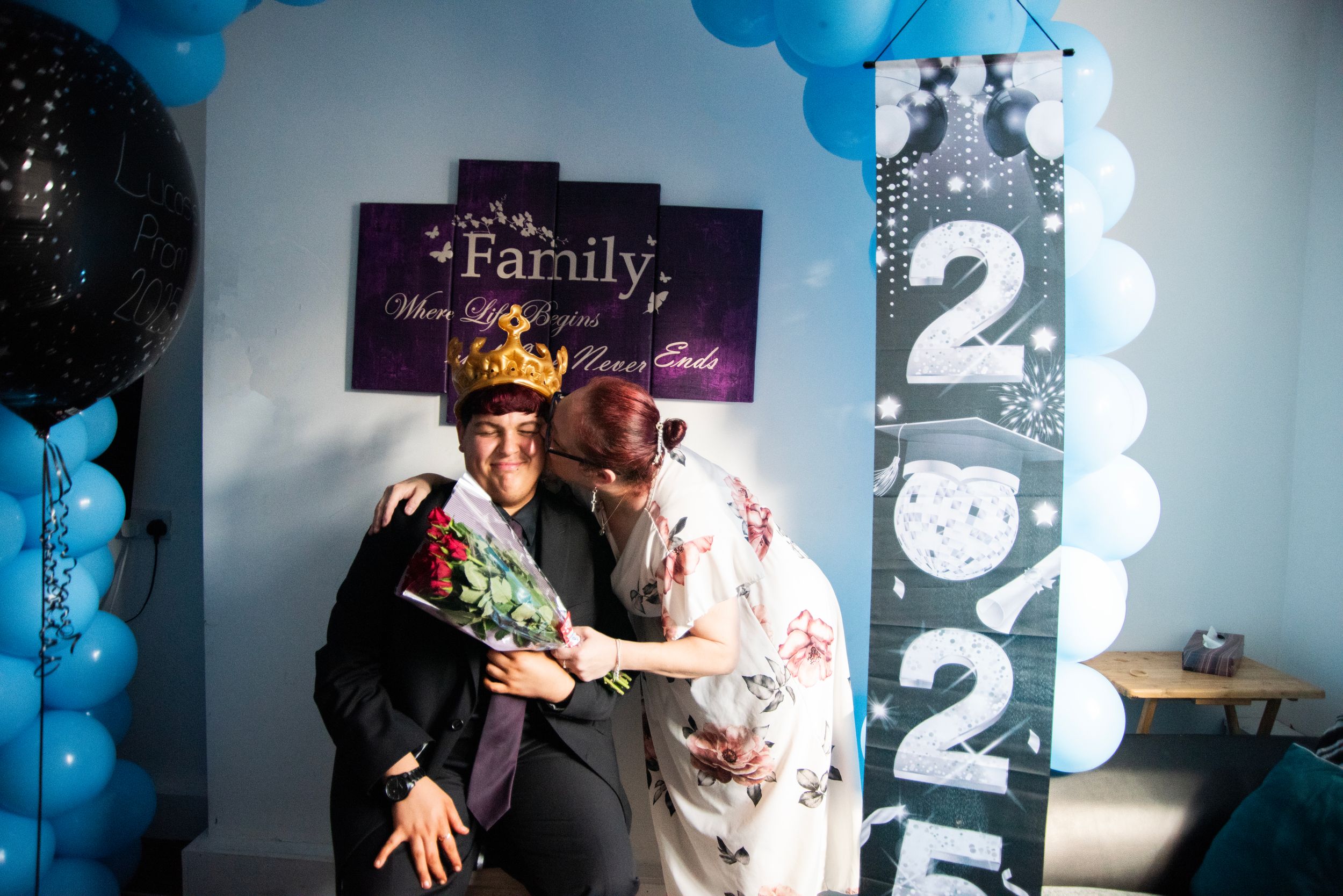Two people share a joyful moment at a New Years celebration with blue balloons and "2023" decor in the background.