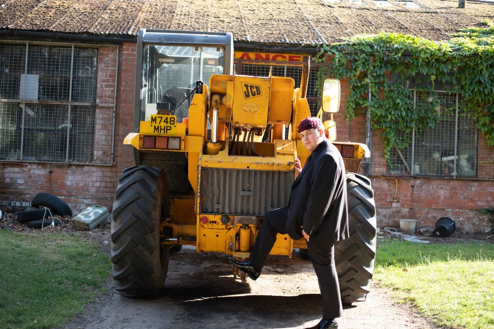 A person operates a yellow construction backhoe near a building with brick walls during daytime.