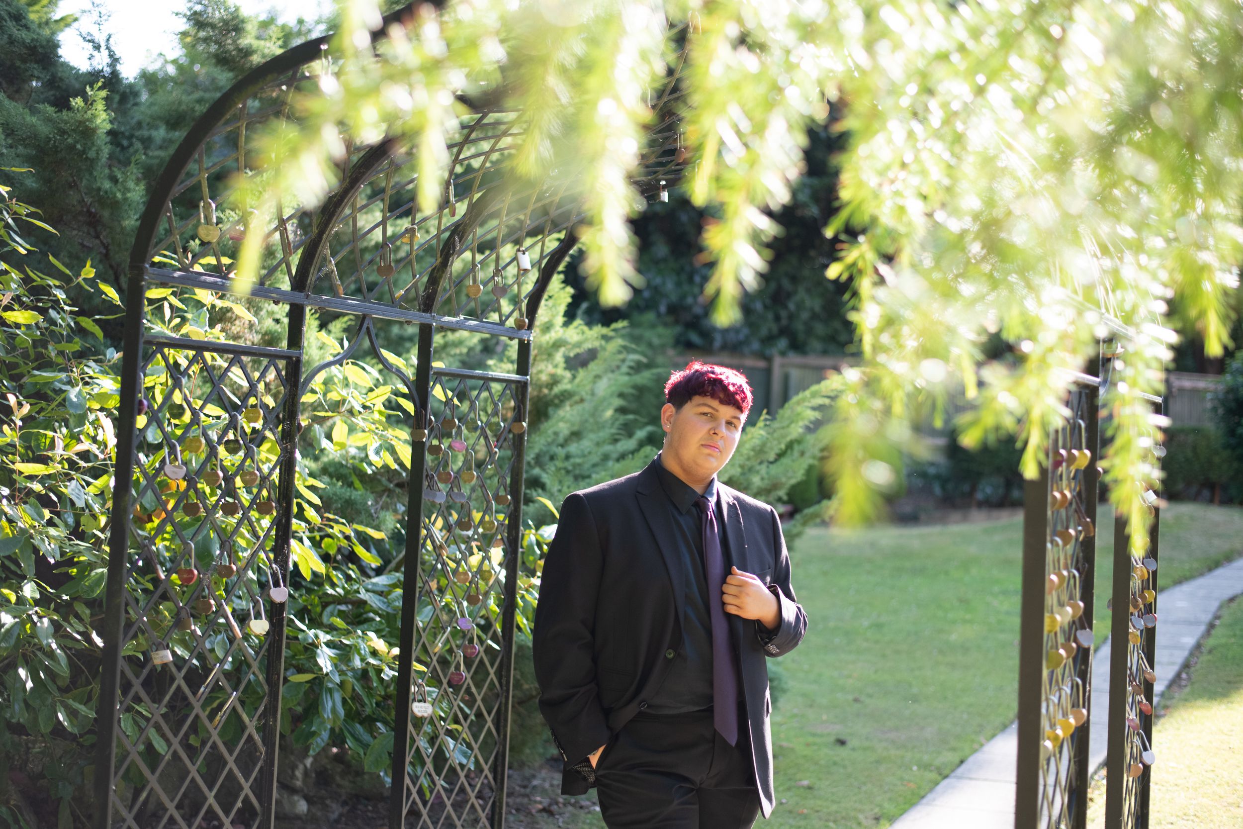 A person in a dark jacket stands beneath blooming yellow wisteria vines in a garden setting during golden hour.