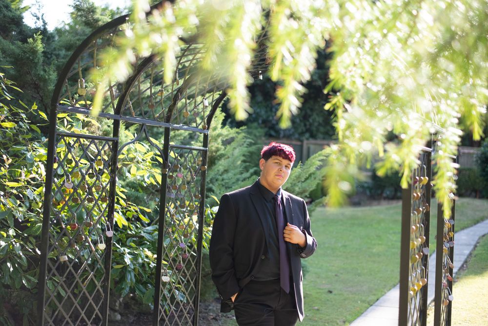 A person in a dark jacket stands beneath blooming yellow wisteria vines in a garden setting during golden hour.