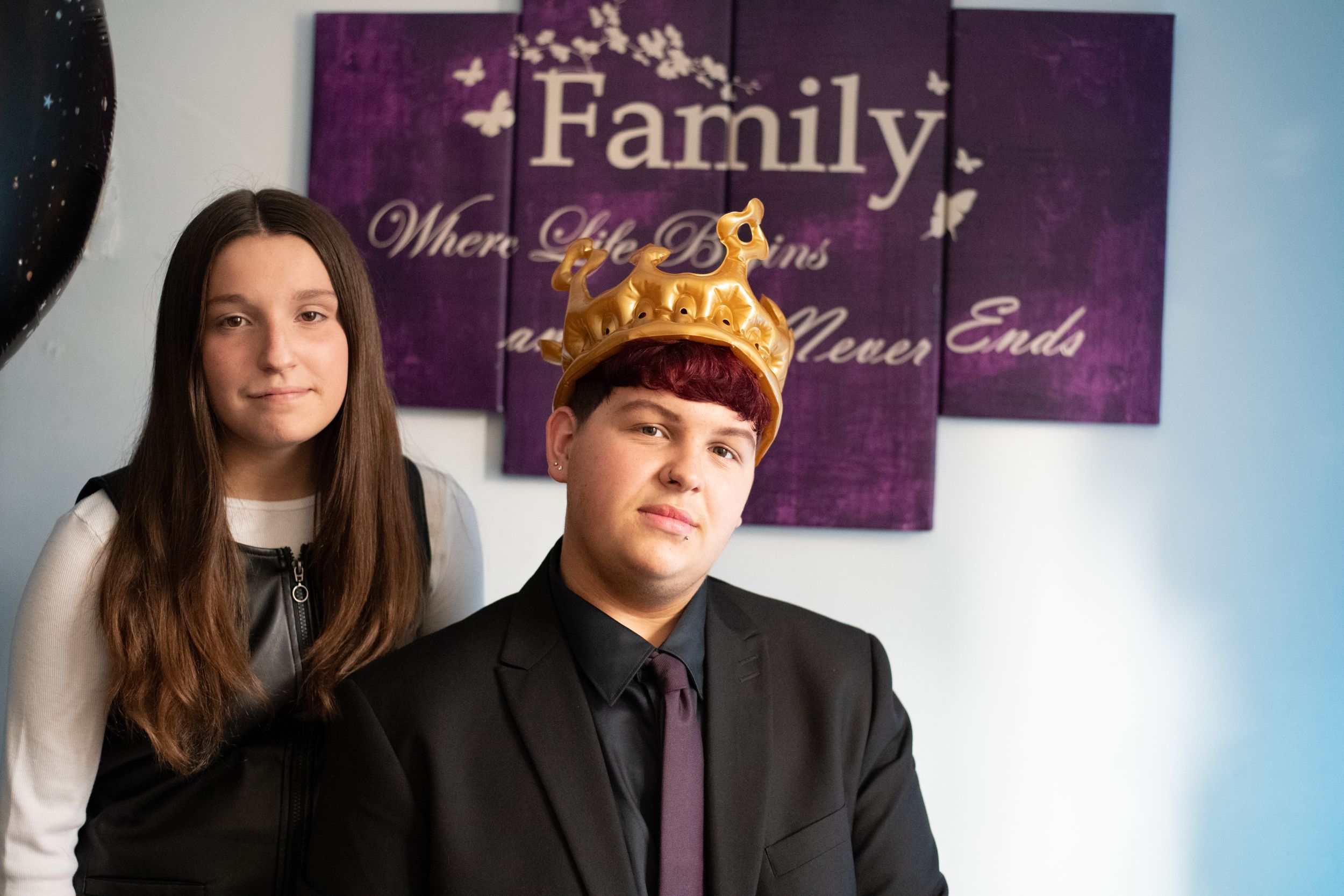 A group in formal attire poses together against a purple wall displaying decorative text in elegant lettering.