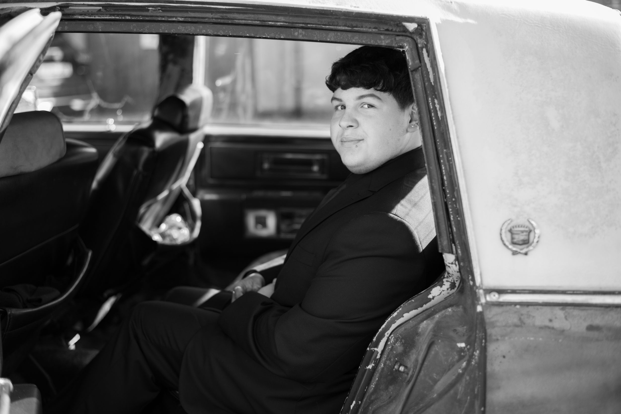 A passenger sits in the back of a vintage Cadillac limousine in this black and white photograph.