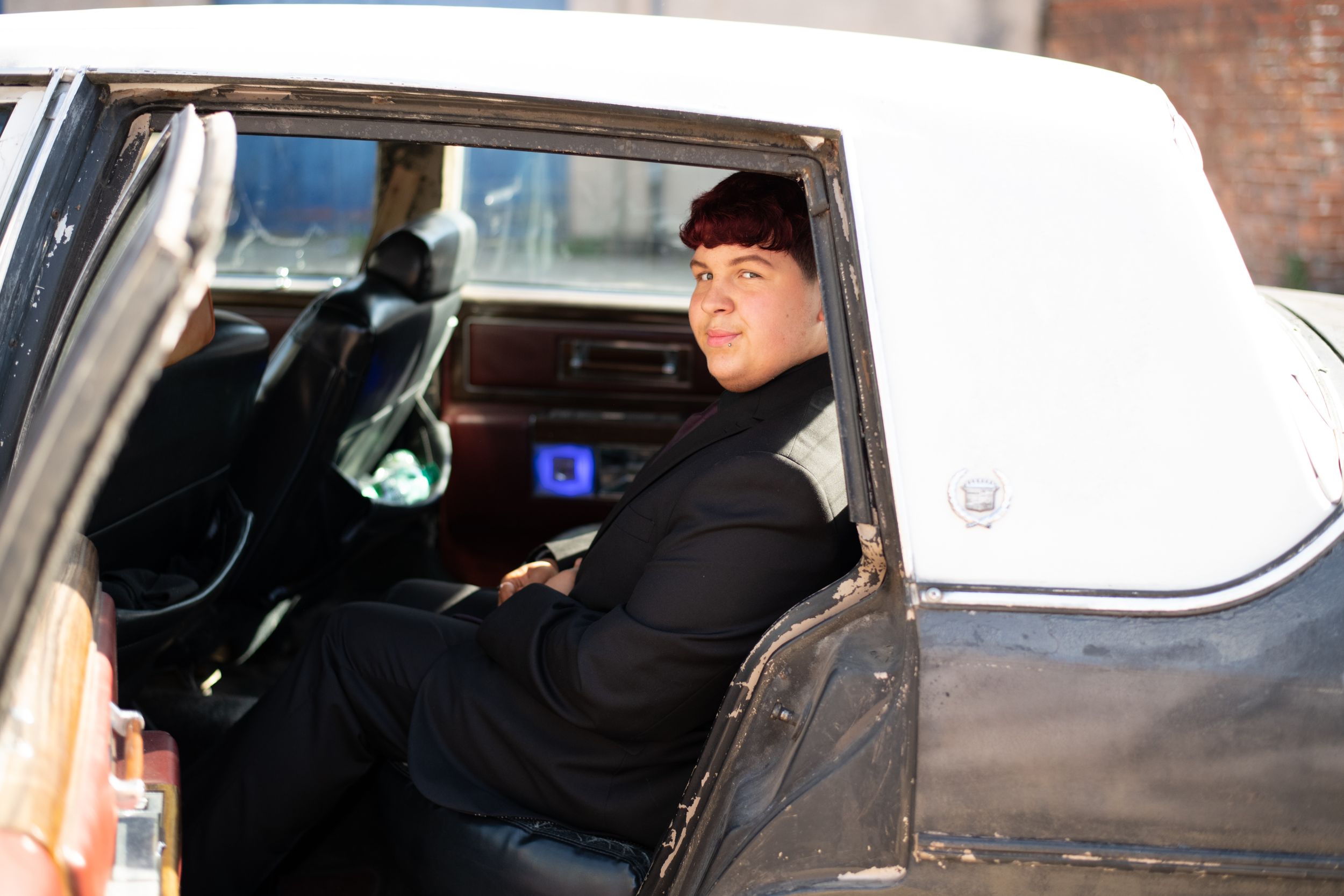 Person in a black coat sits in the back seat of a vintage white and black automobile.