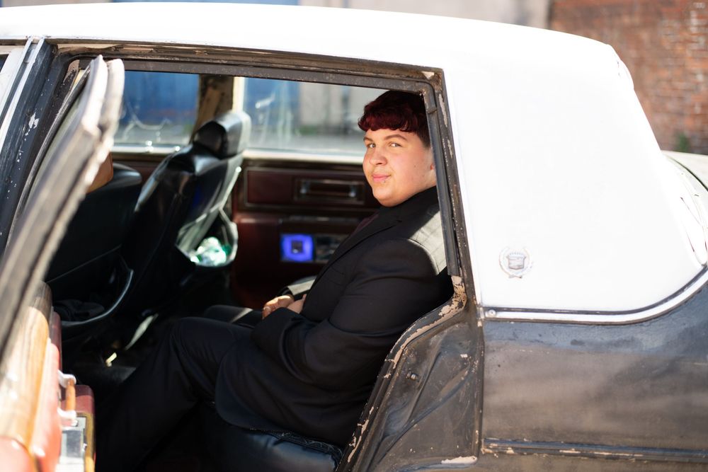 Person in a black coat sits in the back seat of a vintage white and black automobile.
