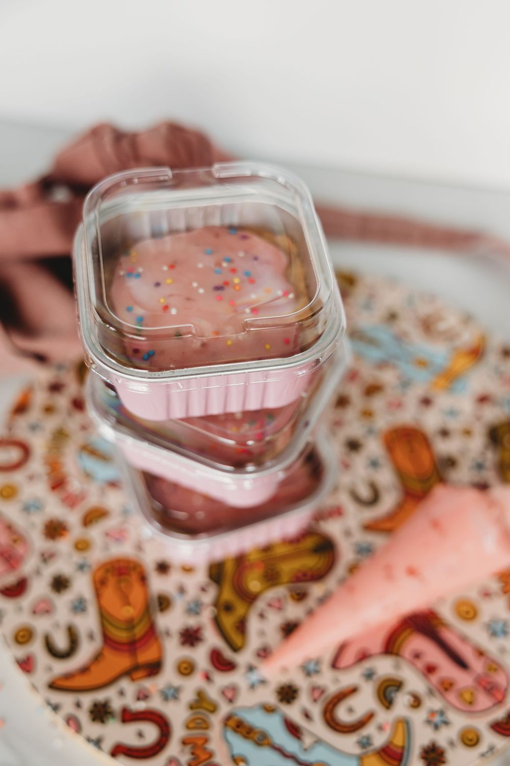 Close-up of a pink heart-shaped dessert garnished with colorful sprinkles on a patterned surface.