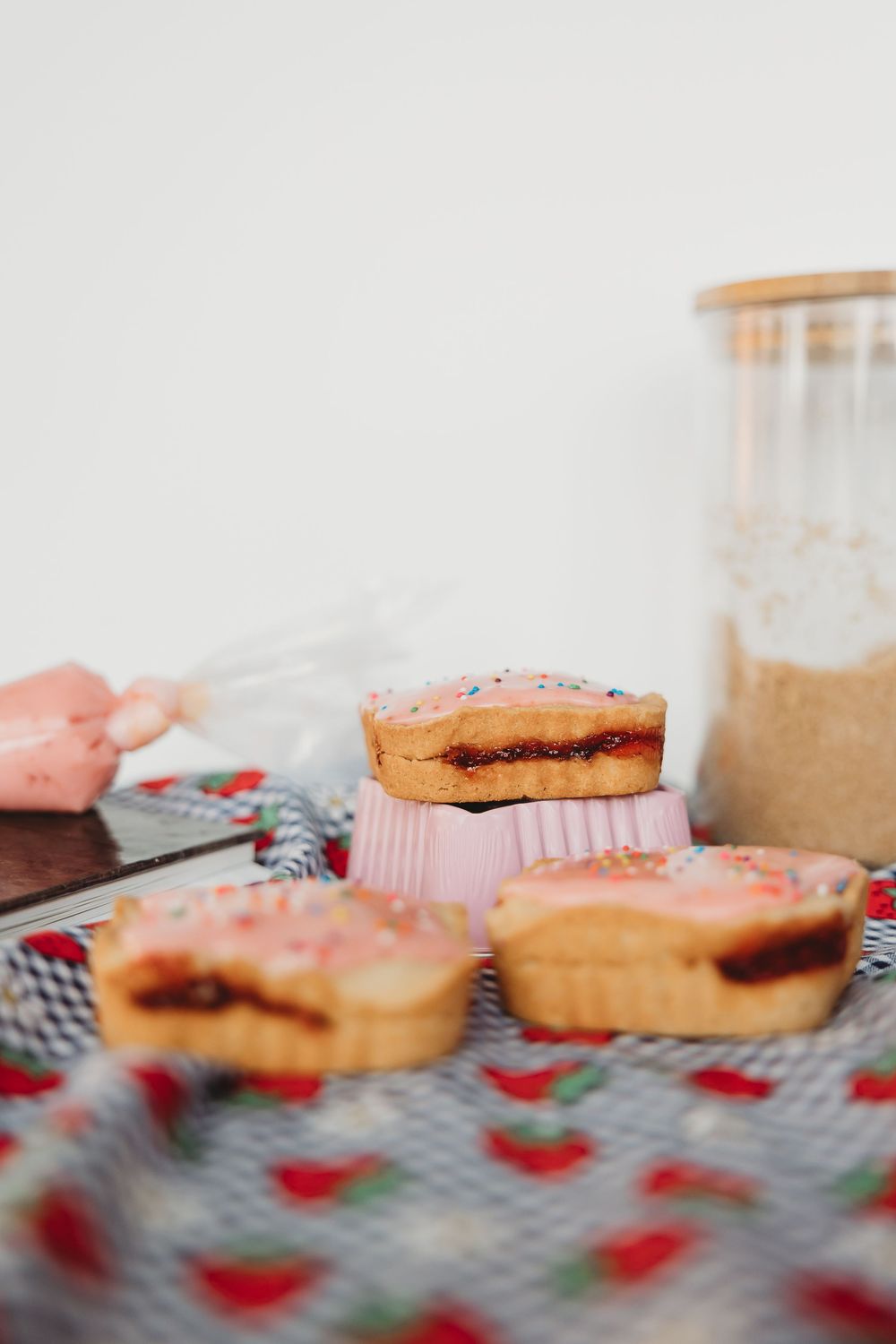 Sugar cookies with pink frosting and red rose petals scattered on a gray checkered surface.