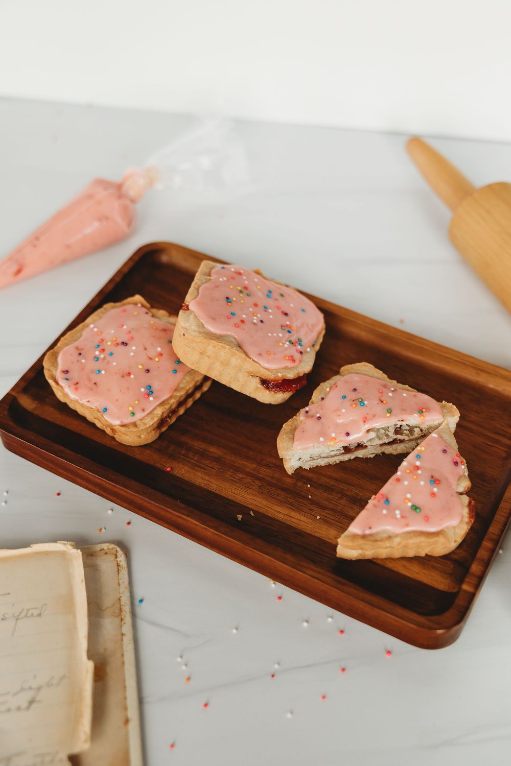 Pink frosted sugar cookies arranged on a rustic wooden serving board with colorful sprinkles and white napkin.